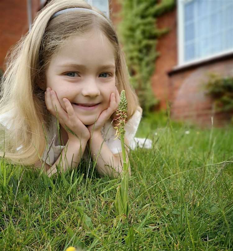 Young child lying on grass looking at a man orchid plant