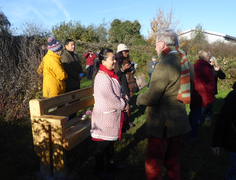 A group of people dressed for winter around a rustic bench in a greenspace